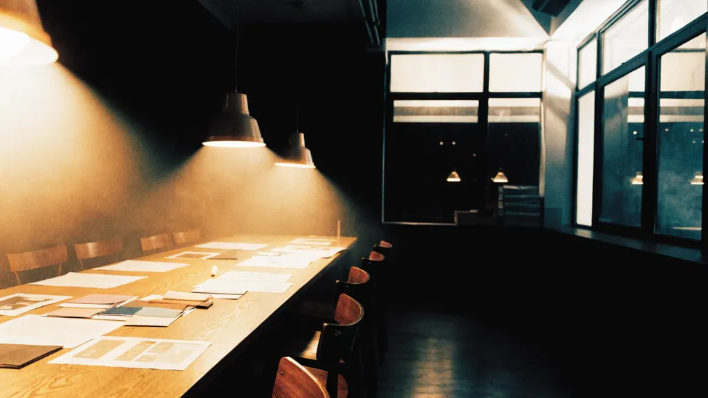 Blick in das MDA-Studio bei Nacht: langer Eichentisch, Layouts und Stoffmuster unter warmen Pendelleuchten